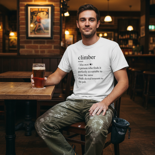Man sitting at a bar holding a beer, wearing a t-shirt with text.